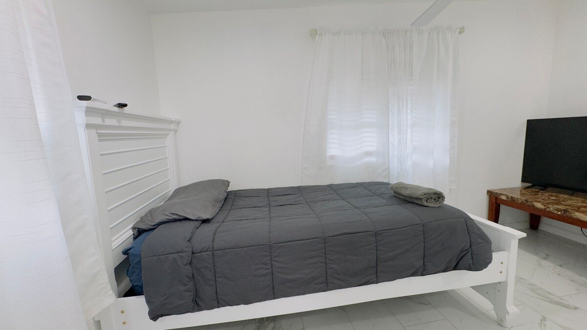 Studio bed with gray bedding and sheer curtains