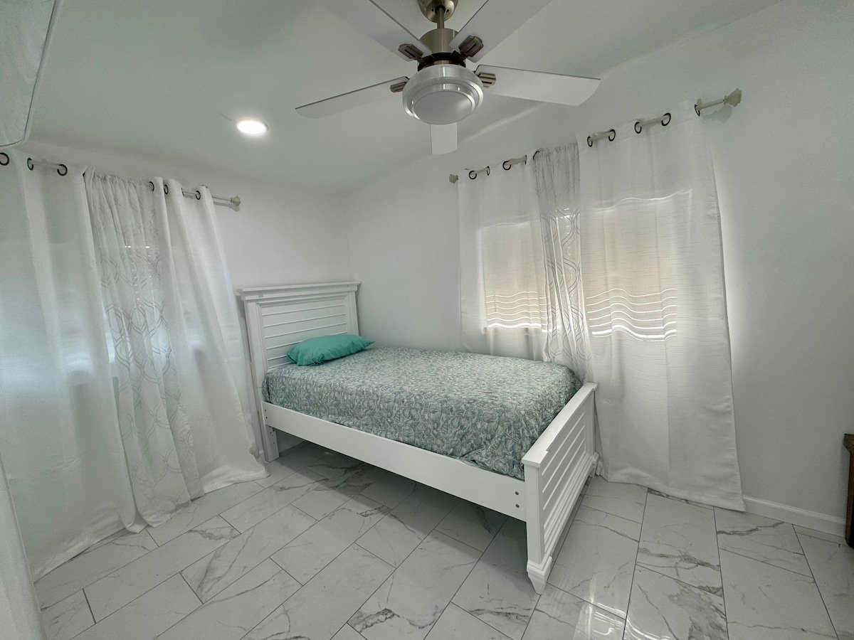 Studio bed with ceiling fan and curtained windows