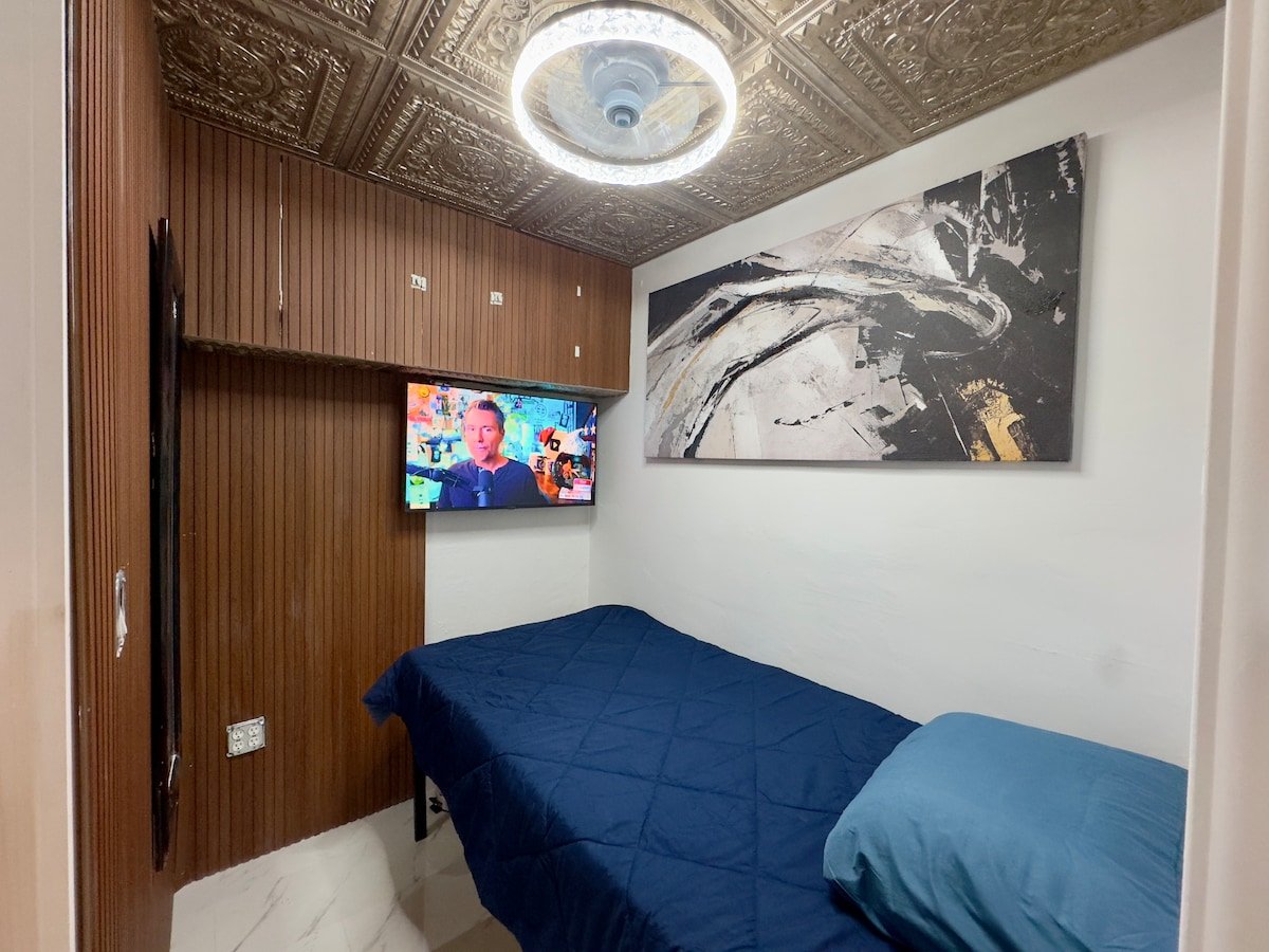 Tiny Room with a twin bed, wall-mounted TV and ring ceiling light